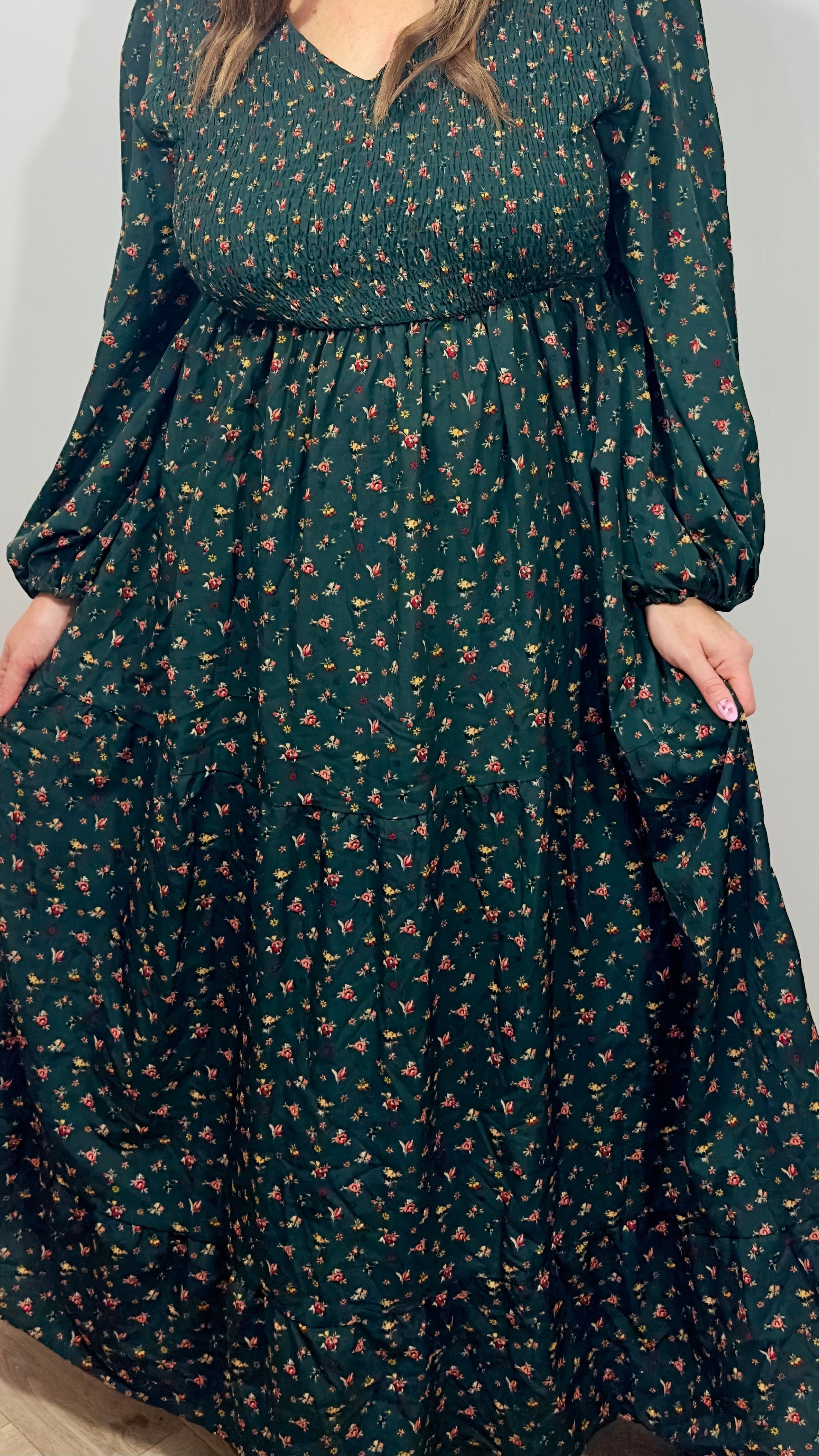 Green dress with floral pattern worn by a person against a plain background