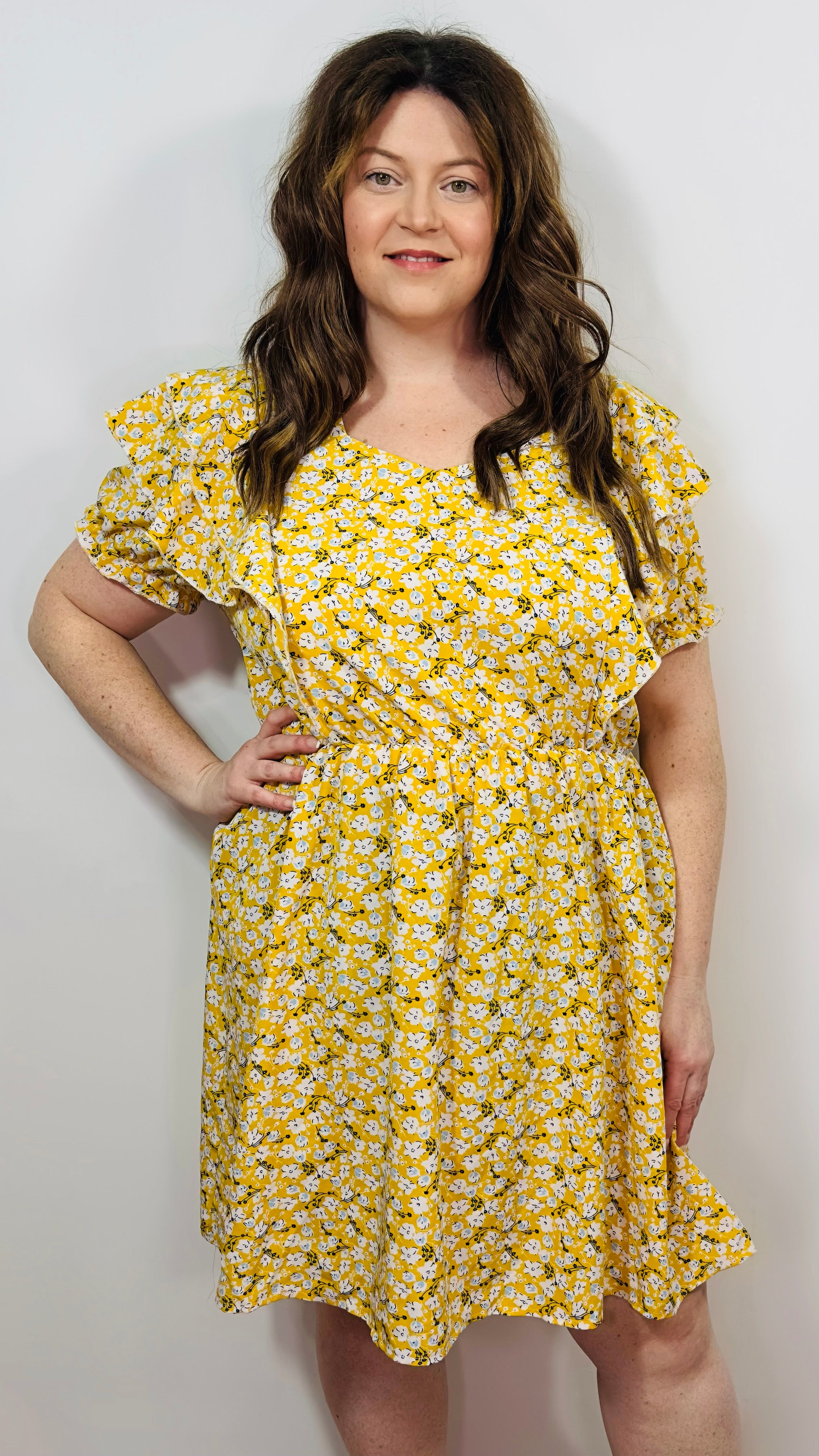 Woman wearing a yellow floral dress against a plain background