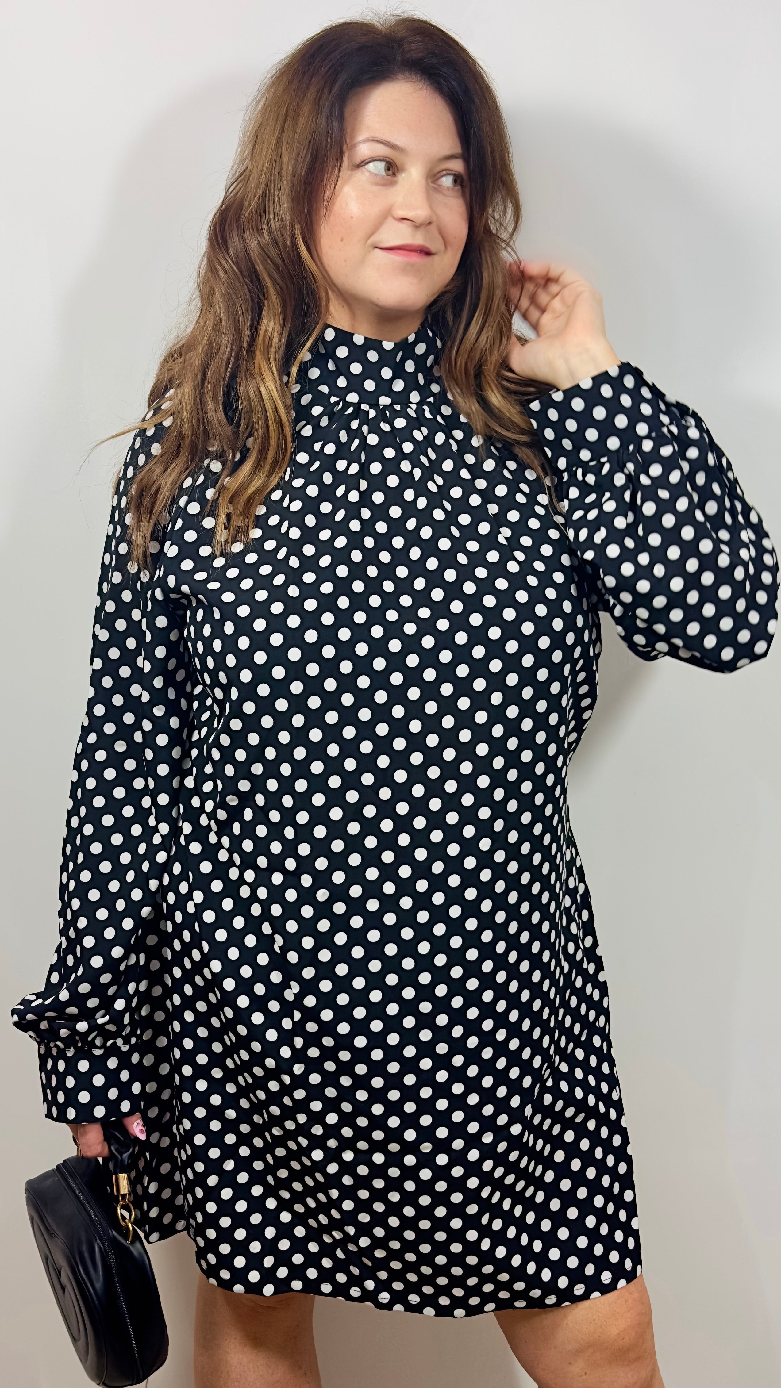 Woman wearing a black polka dot dress against a plain background