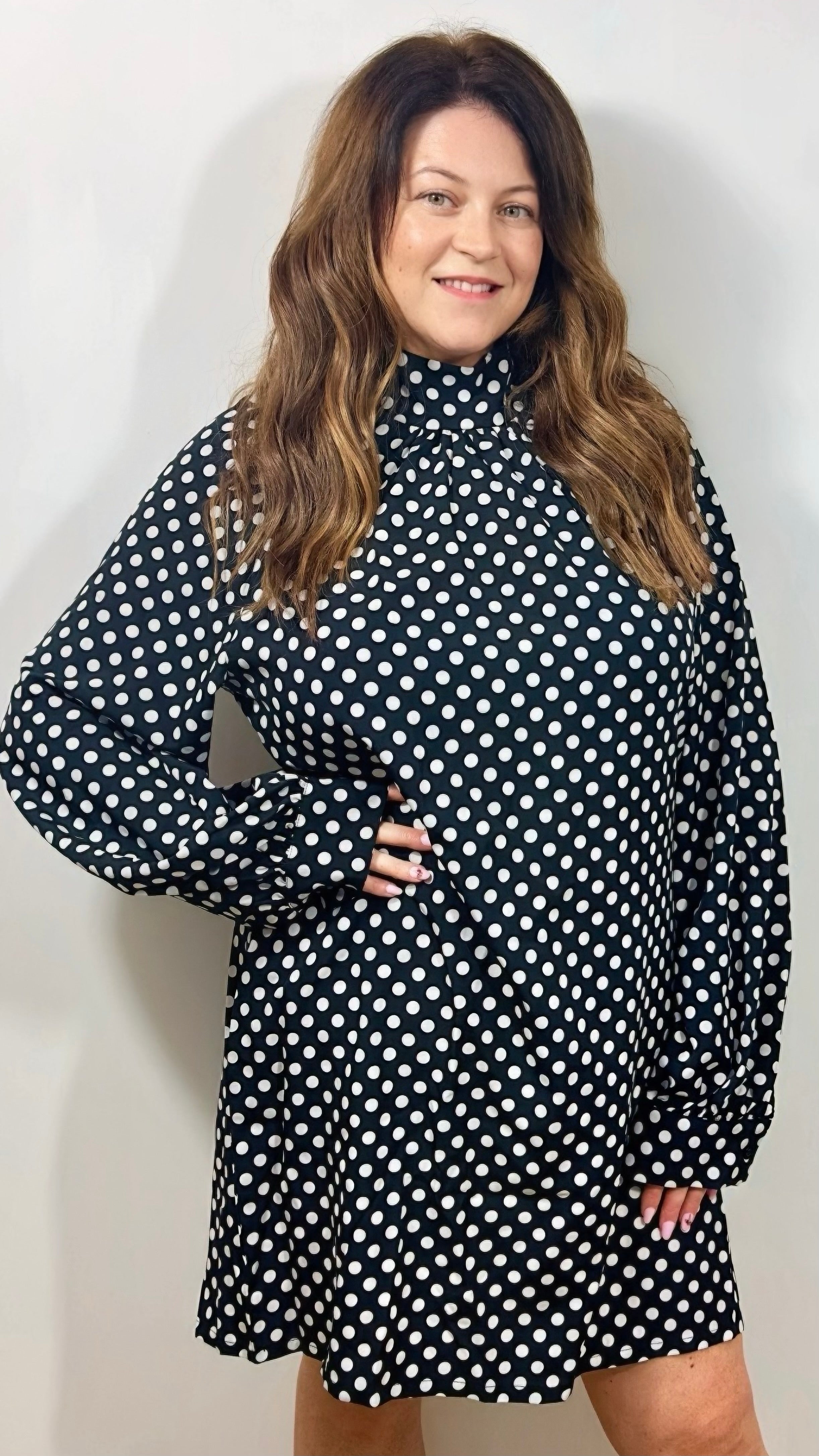 Woman wearing a black polka dot dress against a plain background