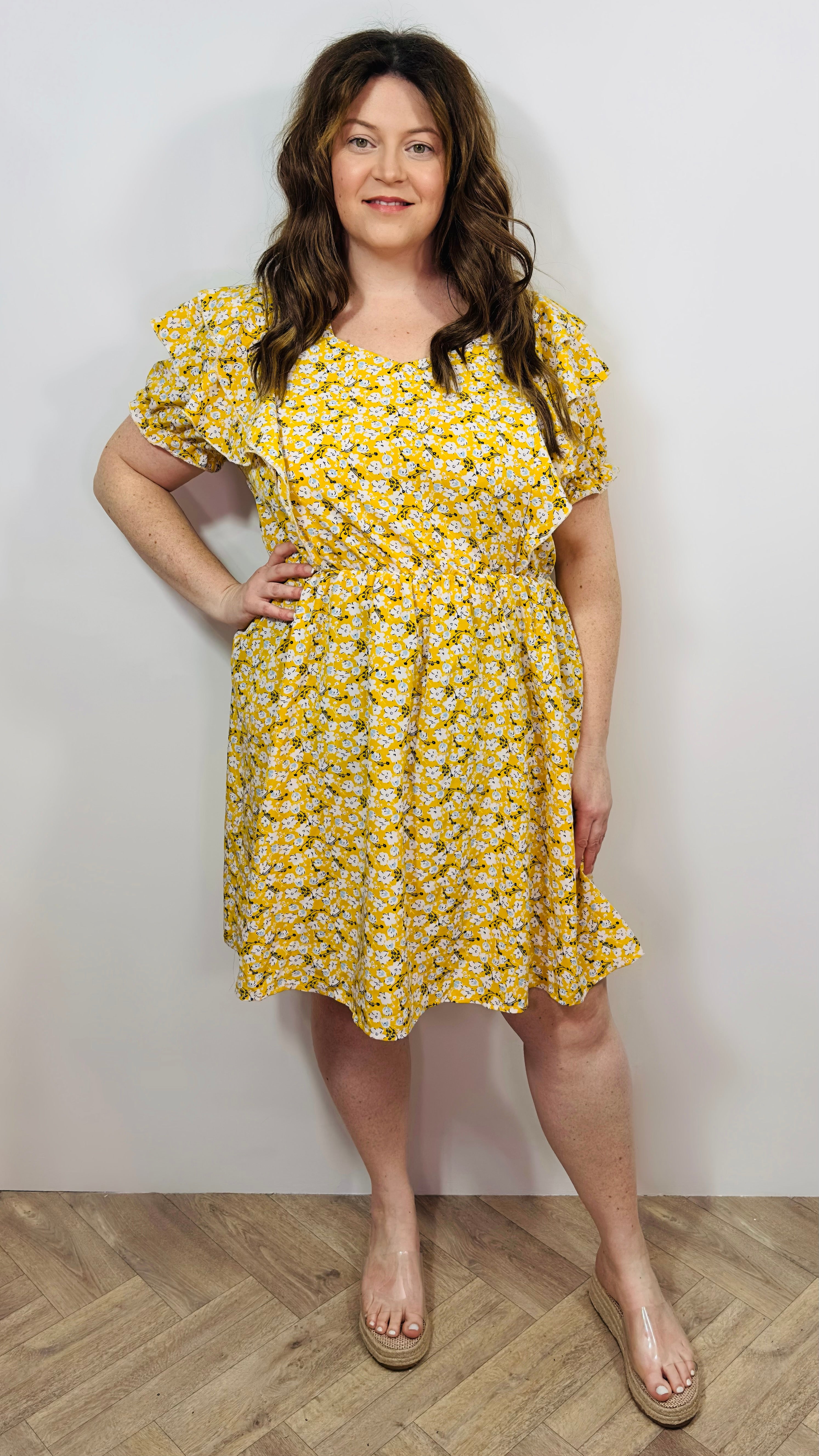Woman wearing a yellow floral dress against a plain background